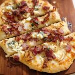 A close-up of a delicious 10-ingredient pizza with bacon, blue cheese, and thinly sliced onions on a wooden board.