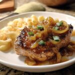 A juicy pork chop topped with caramelized onions and green onions, served with pasta.
