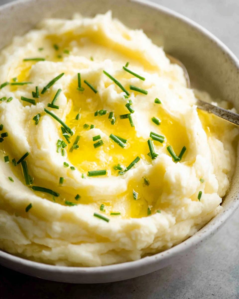 A close-up of creamy 12-Ingredient Mashed Potatoes topped with melted butter and fresh chives.