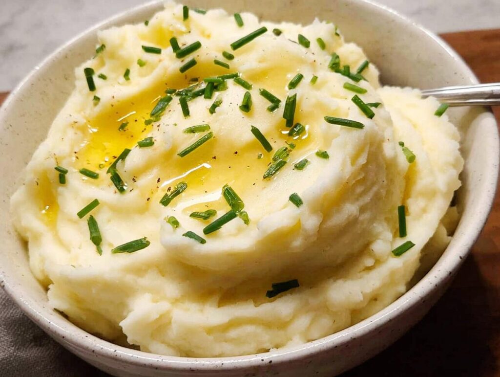Close-up of fluffy 12-Ingredient Mashed Potatoes topped with melted butter and fresh chives.