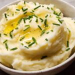 Close-up of fluffy 12-Ingredient Mashed Potatoes topped with melted butter and fresh chives.