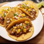Three corn tortillas filled with shredded meat, topped with mango salsa, red onion, cilantro, and crumbled cheese for 12-Ingredient Taco Tuesday Recipes.