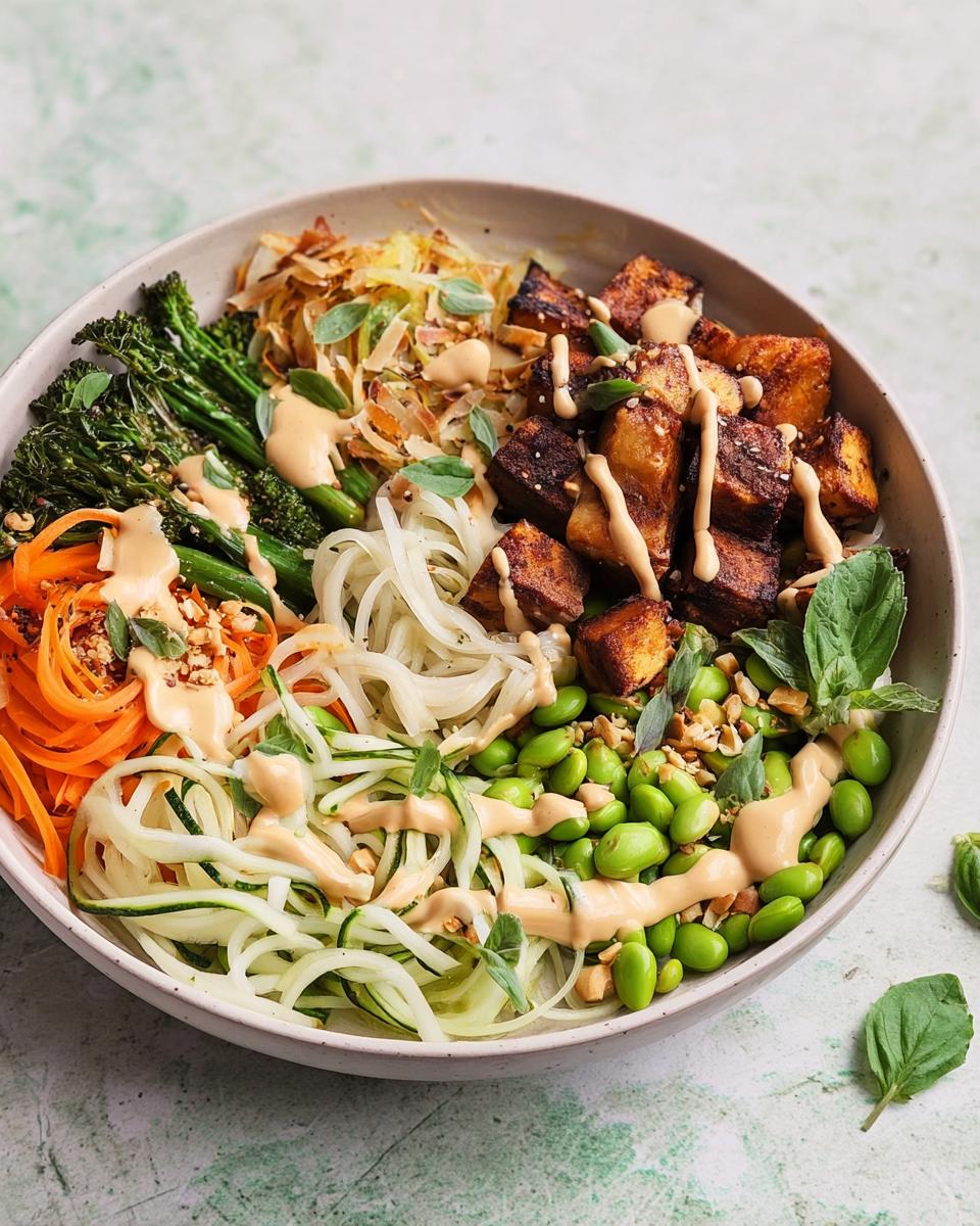 A vibrant bowl of 20-ingredient rice bowls recipe featuring tofu, edamame, carrots, zucchini noodles, and broccolini with a creamy dressing.