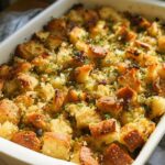 Close-up of a golden brown 7-ingredient stuffing recipe baked in a white ceramic dish, garnished with fresh herbs.