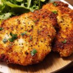 Two golden-brown, crispy air fryer chicken breasts garnished with parsley, served with lemon wedges and a side salad.