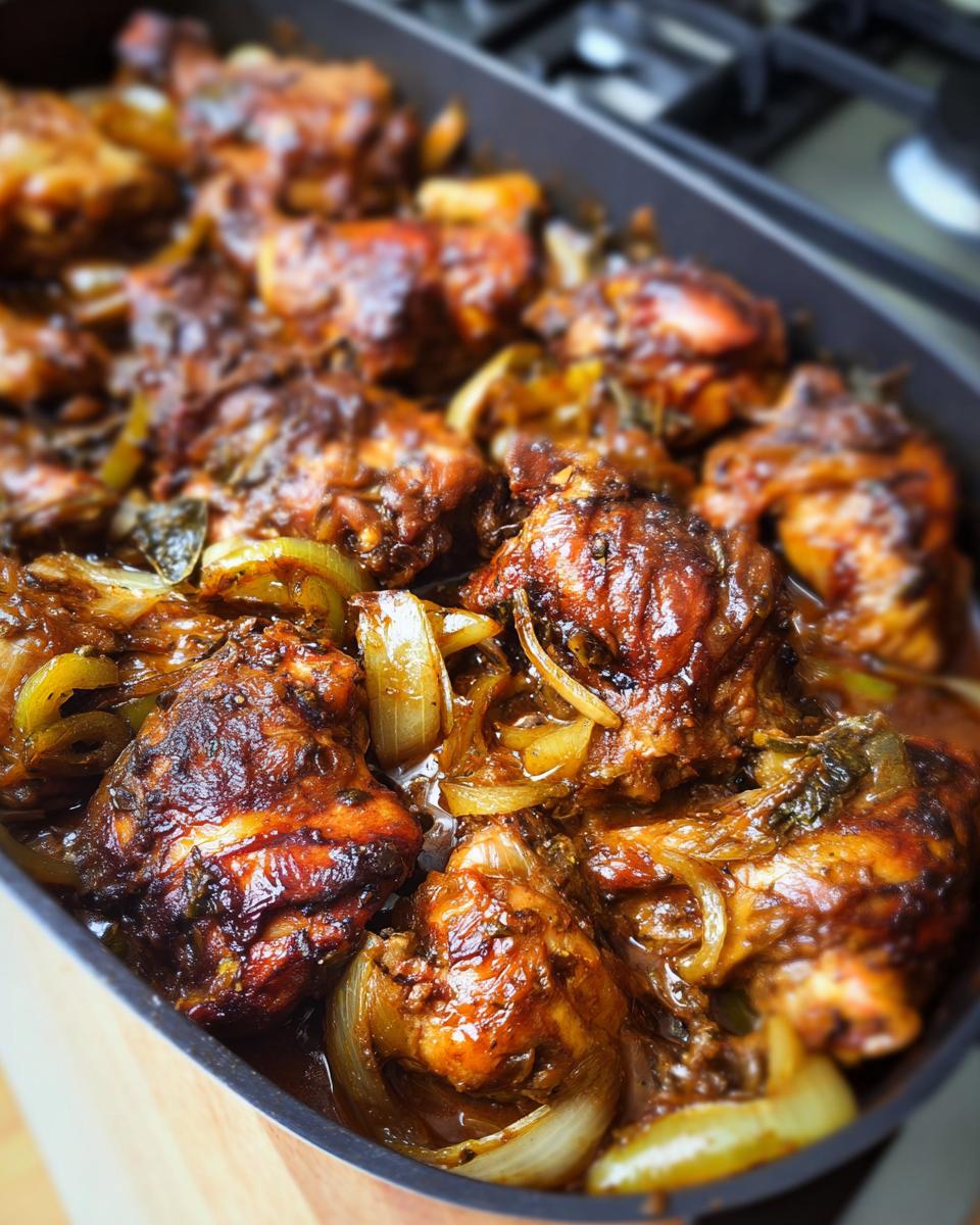 Close-up of juicy baked chicken pieces with caramelized onions in a dark baking dish, part of amazing chicken recipes.