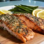 Two perfectly baked salmon fillets seasoned with herbs, served with lemon slices and green beans.