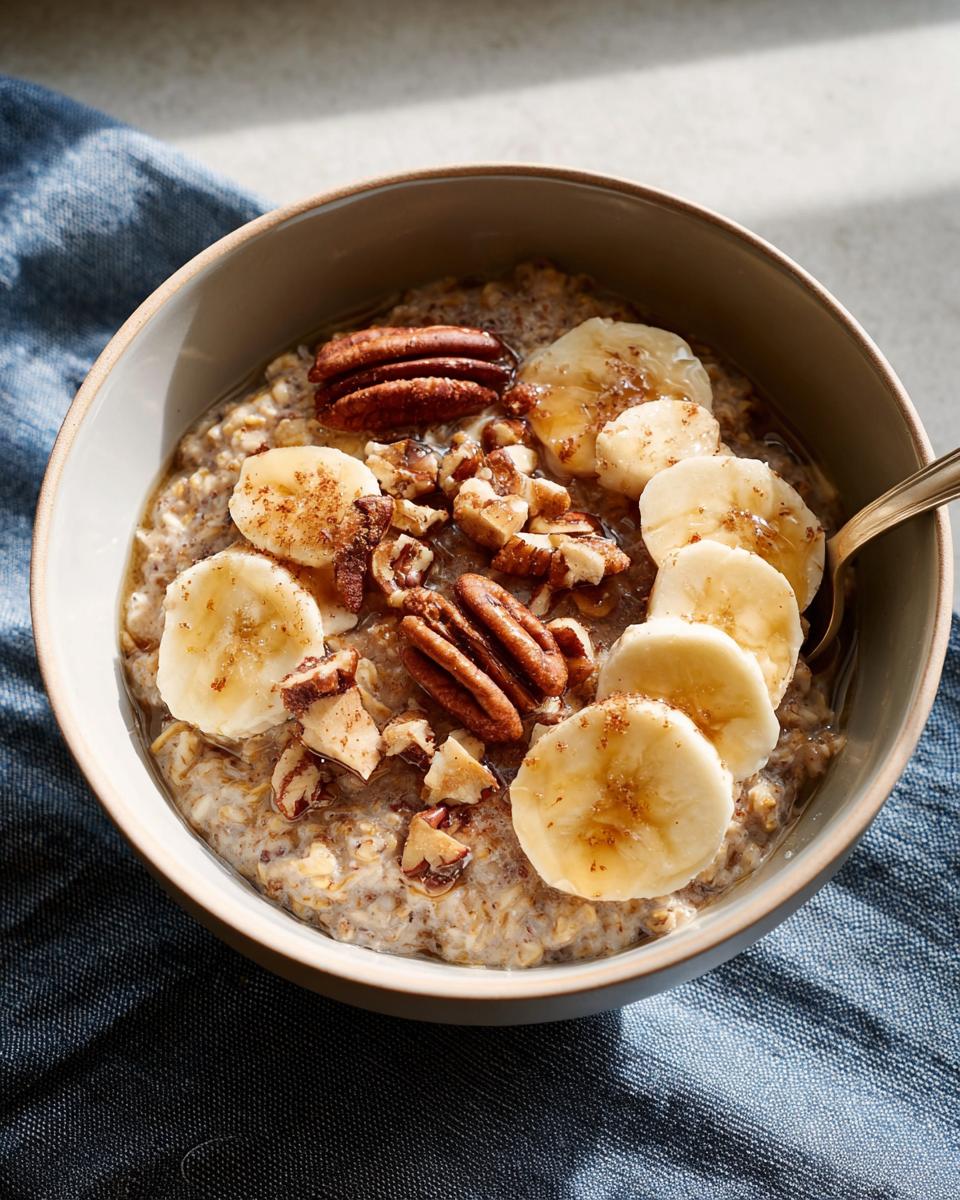 A bowl of oatmeal topped with banana slices, pecans, and a drizzle of honey, perfect for one of our 12 genius breakfast ideas.
