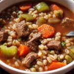 Close-up of a bowl of hearty beef barley soup, featuring tender beef chunks, barley, carrots, and celery.