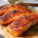 Three perfectly cooked salmon fillets seasoned with spices, presented on parchment paper as part of The Ultimate Salmon Recipes Guide for Beginners.