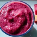 Close-up of a vibrant berry smoothie in a glass, with chunks of fruit on the side. A perfect addition to your breakfast ideas recipes.