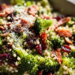 Close-up of a vibrant broccoli couscous salad with cranberries, bacon, and grated Parmesan cheese.