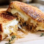 A perfectly grilled cheese sandwich with melted cheese and caramelized onions, cut in half to show the gooey interior.