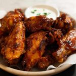 A close-up of glossy, saucy chicken wings served with a side of dipping sauce, perfect for quick Chicken Wings Recipes in 20 Minutes.