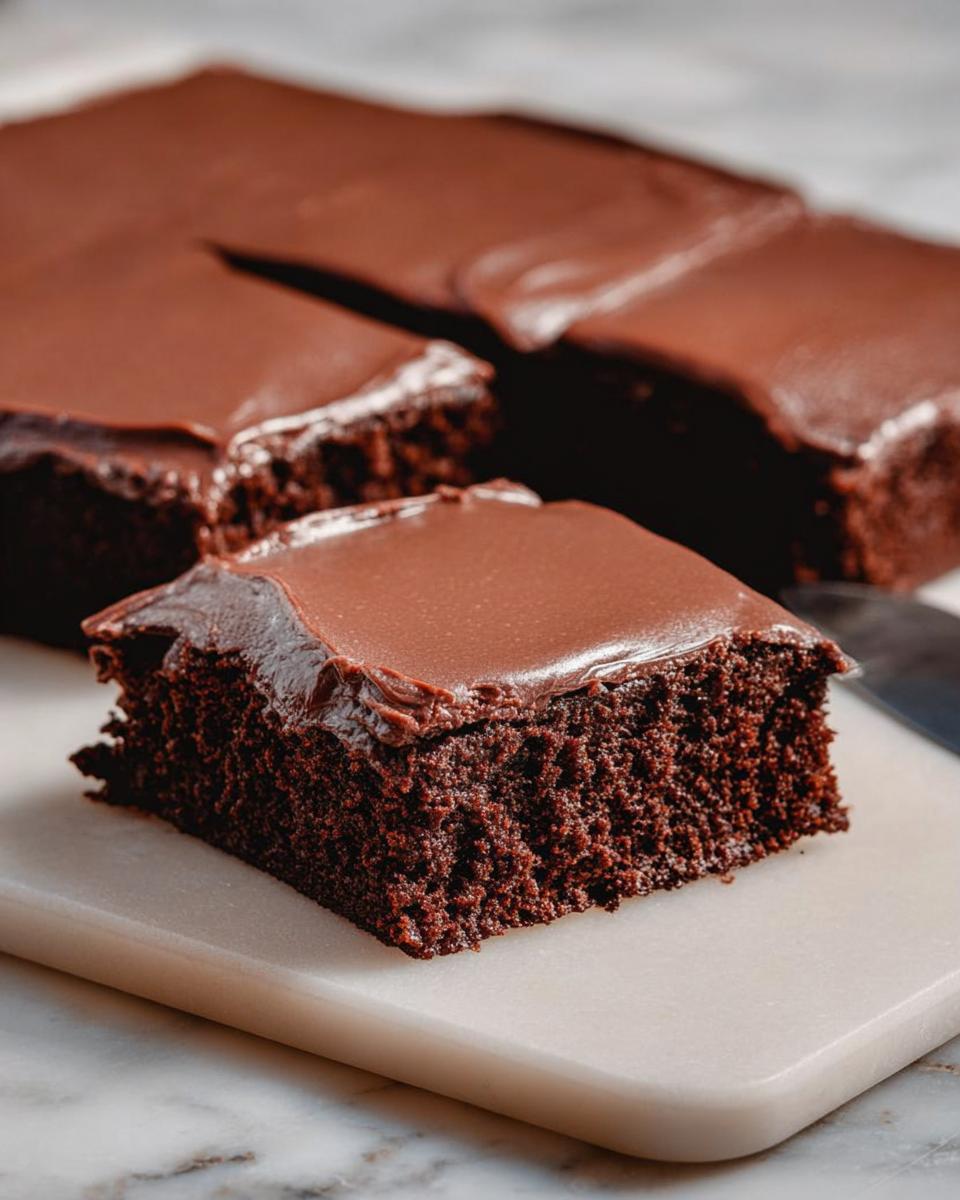 A moist slice of chocolate cake with rich chocolate frosting, part of a larger cake.