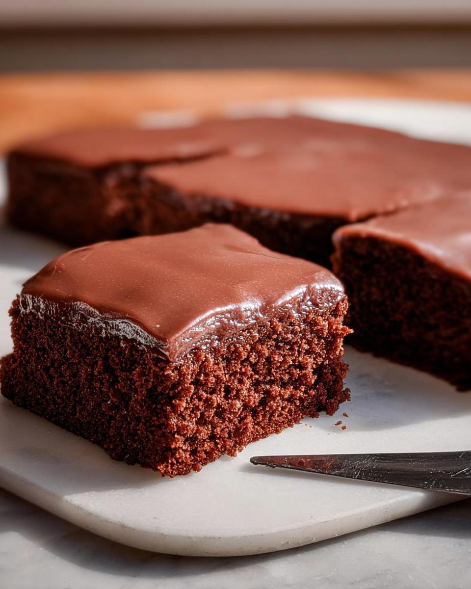 Close-up of a rich chocolate cake slice with smooth frosting, showcasing its moist texture. Part of cake ideas recipes.