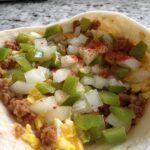 Close-up of a breakfast burrito filled with scrambled eggs, sausage, diced green peppers, and onions, sprinkled with paprika.
