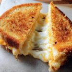 A perfectly grilled cheese recipe sandwich, cut in half, with melted cheese oozing out.
