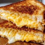 Close-up of a perfectly grilled cheese sandwich, oozing with melted cheese, cut in half.