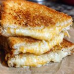 Close-up of a stack of golden-brown grilled cheese sandwiches, oozing with melted cheese. Perfect for quick weeknight meals.