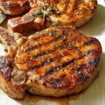 Close-up of perfectly grilled pork chops with grill marks and seasoned with herbs.