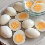 A plate and bowl filled with hard-boiled eggs, some whole and some halved, showcasing their bright yellow yolks. Perfect for Healthy Meals Recipes Meal Prep.