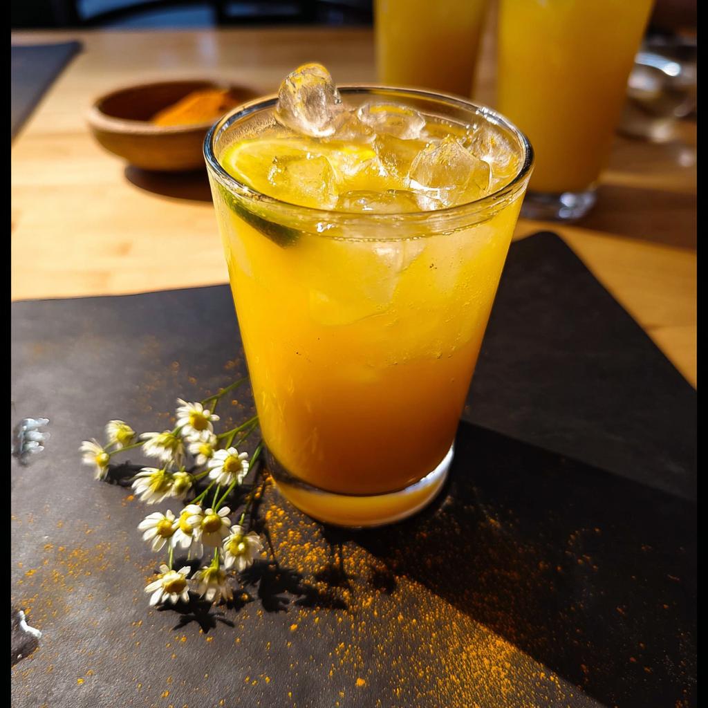 A refreshing orange drink with ice and lime, garnished with small white flowers and turmeric powder.