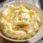 A bowl of creamy Keto Mashed Potatoes topped with butter, herbs, and black pepper.