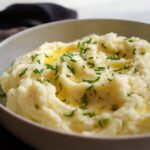 A close-up of fluffy mashed potatoes topped with melted butter and fresh chives, perfect for beginners.