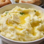 Close-up of a bowl of creamy mashed potatoes topped with a pat of butter, melted butter, and black pepper.