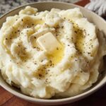 A bowl of creamy mashed potatoes topped with a melting pat of butter and cracked black pepper.