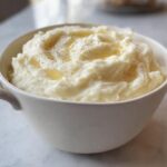 A bowl of fluffy mashed potatoes, topped with melted butter and black pepper, perfect for meal prep.