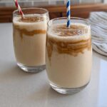 Two glasses of creamy peanut butter smoothie with swirls of peanut butter and colorful straws, part of beginner breakfast ideas.