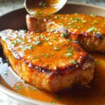 Close-up of two perfectly cooked pork chops bathed in a rich, glossy sauce and sprinkled with fresh herbs.