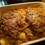 Two juicy pork chops baked in a casserole dish with sauerkraut and potatoes, a quick weeknight meal.