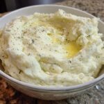 A bowl of creamy mashed potatoes with melted butter and herbs, perfect for a pro mashed potatoes recipe.