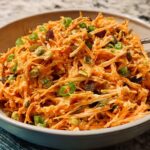 A bowl of shredded carrot salad with raisins, green onions, and a creamy dressing, perfect for quick veggie sides recipes.
