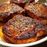 Close-up of perfectly seared restaurant-style pork chops, glistening with juices and seasoned with herbs.
