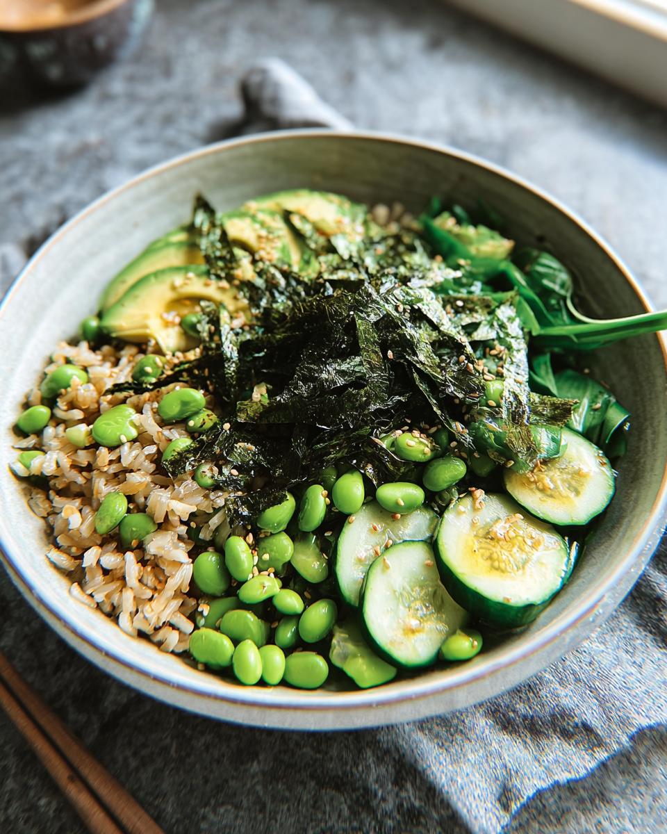 A healthy and flavorful rice bowl featuring brown rice, sliced avocado, edamame, cucumber, and nori seaweed.