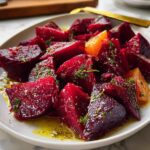 A vibrant plate of roasted beet salad with orange segments, drizzled with olive oil and sprinkled with fresh herbs, showcasing a perfect veggie side recipe.