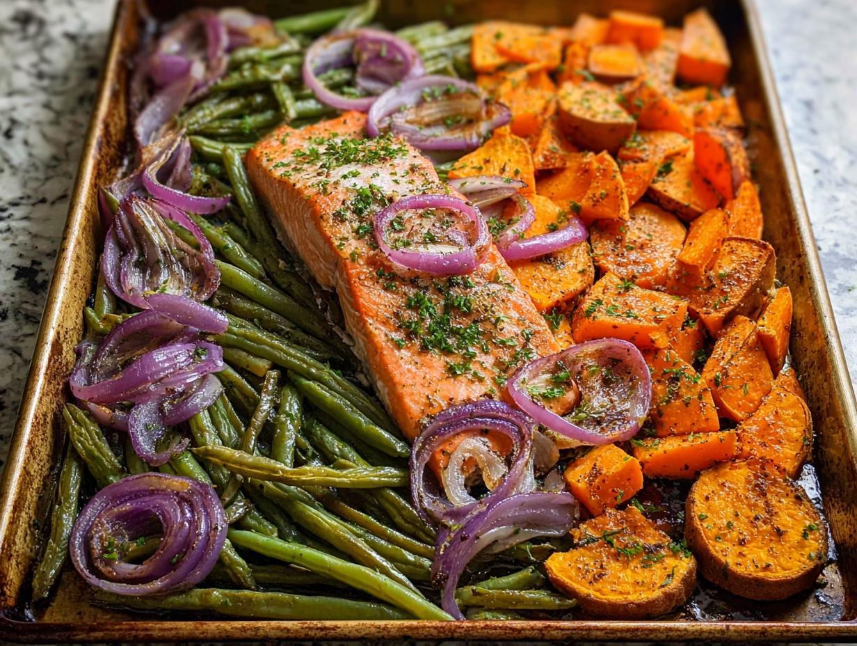 Sheet pan meal prep with salmon, green beans, sweet potatoes, and red onion, seasoned with herbs.