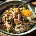A close-up of a salmon rice bowls recipe with a fried egg, corn, broccoli, and sesame seeds.