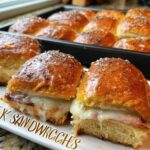 Two savory sandwich ideas recipes with melted cheese and ham on a white plate, with more sandwiches in a baking pan behind.