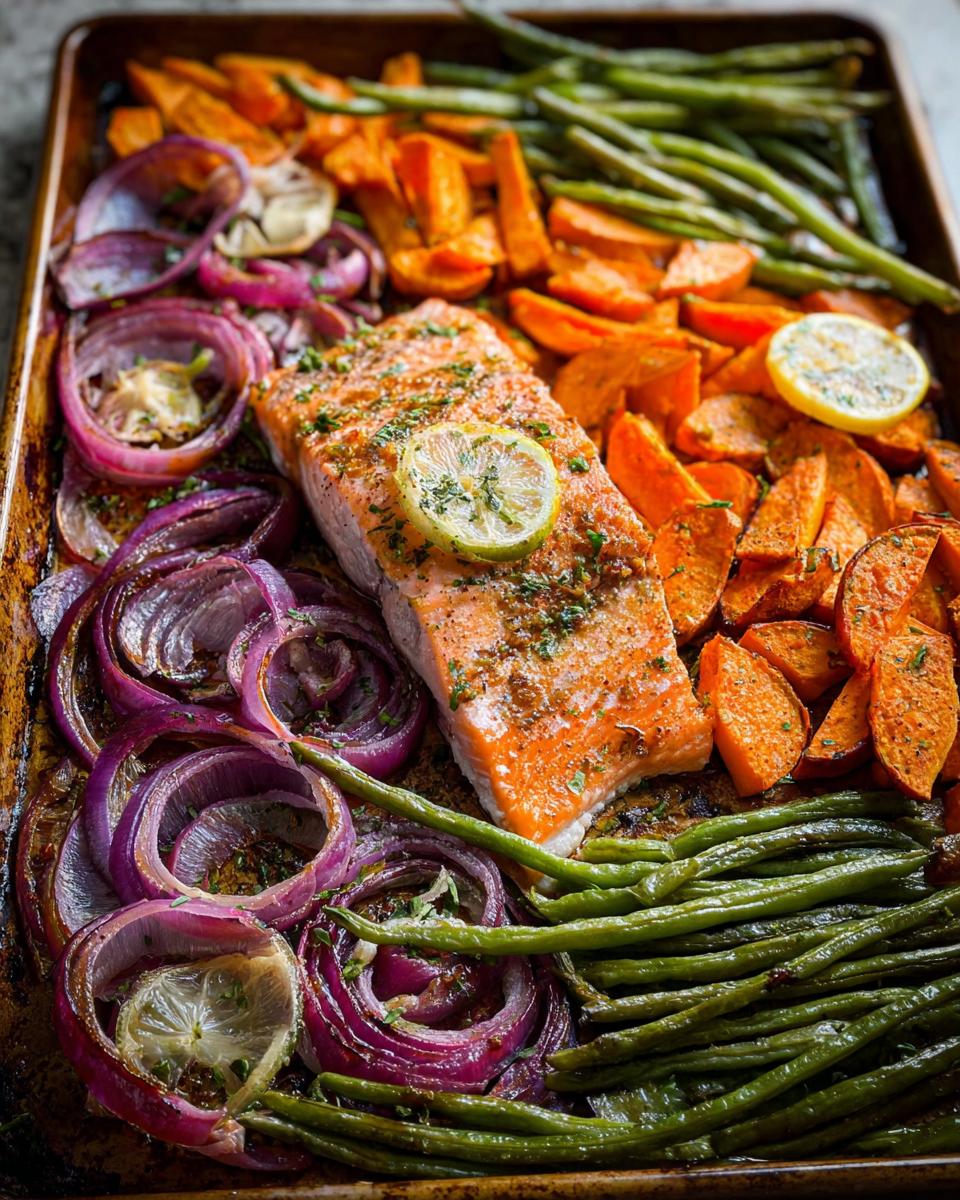 A delicious sheet pan meal prep featuring a salmon fillet surrounded by roasted sweet potatoes, red onions, and green beans.