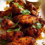 Close-up of a platter of glistening, spicy chicken wings, garnished with fresh herbs.