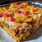 A hearty slice of Taco Tuesday casserole featuring layers of ground meat, corn, cheese, and crushed tortilla chips, topped with diced tomatoes.