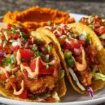 Three crispy tacos filled with fried fish, lettuce, pico de gallo, and a drizzle of sauce, served with mashed sweet potatoes.