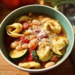 A steaming bowl of tortellini soup with white beans, zucchini, tomatoes, and cheese, perfect for busy weeknights.