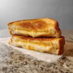 Two halves of a perfectly golden-brown grilled cheese sandwich, with melted cheese oozing out.