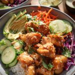 A close-up of a vibrant Bang Bang Chicken Bowl featuring crispy chicken, rice, avocado, cucumber, and shredded carrots.